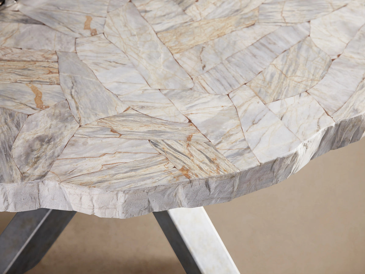 Petra Round Dining Table with a textured, polished stone top and a sturdy iron base forming an X shape, on a wooden floor.