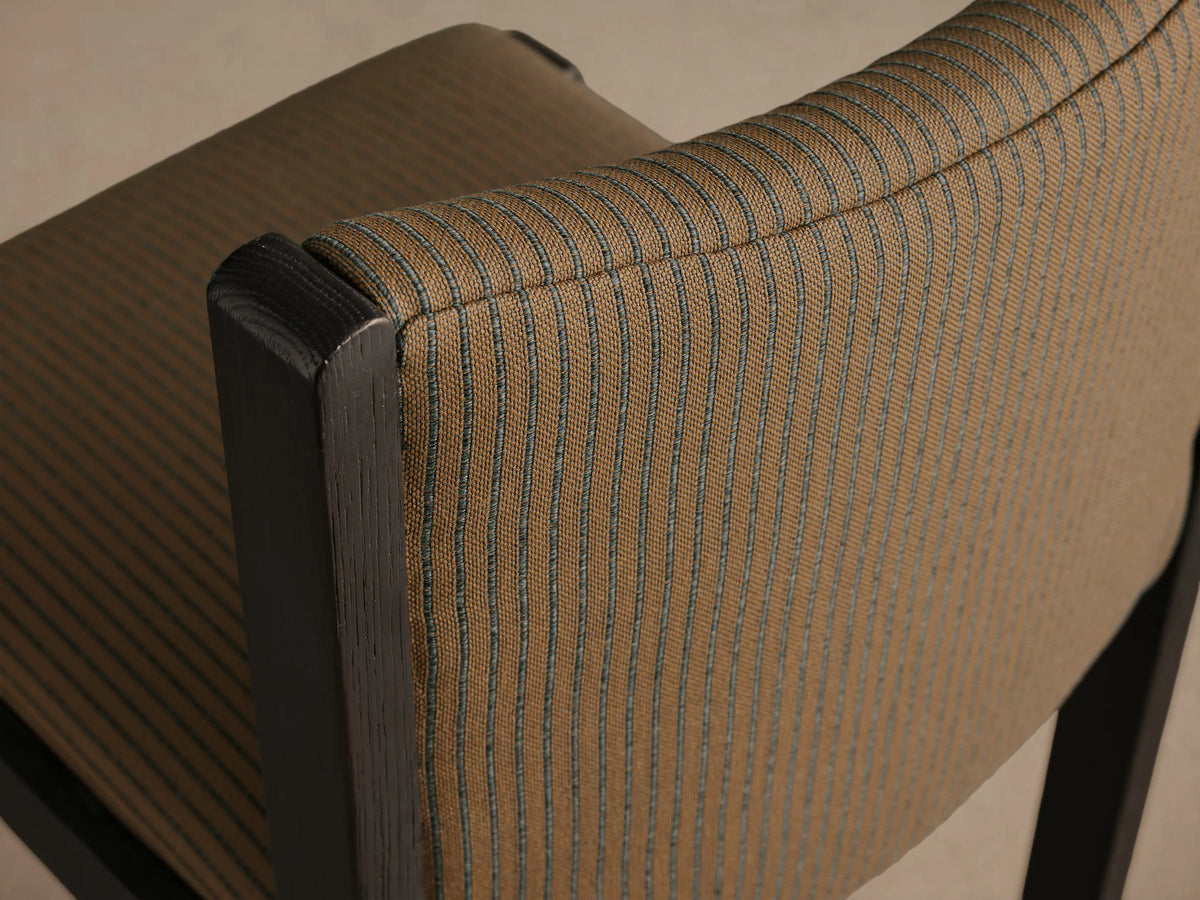 Paradiso Dining Chair, front view. Dark oak wood frame with tan upholstered seat and curved backrest, featuring thin black vertical stripes.
