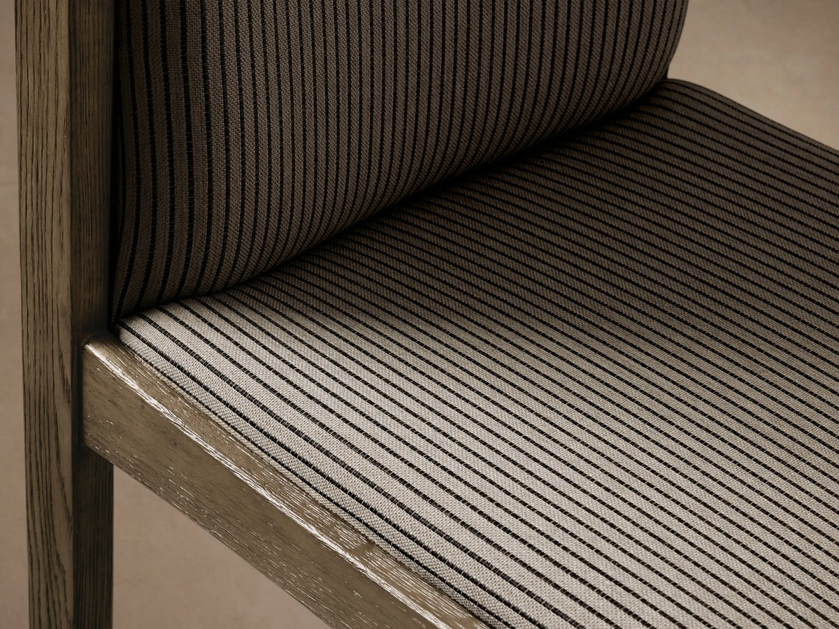Paradiso Dining Chair, front view. Weathered oak frame, beige upholstery with thin black vertical stripes on wood floor.