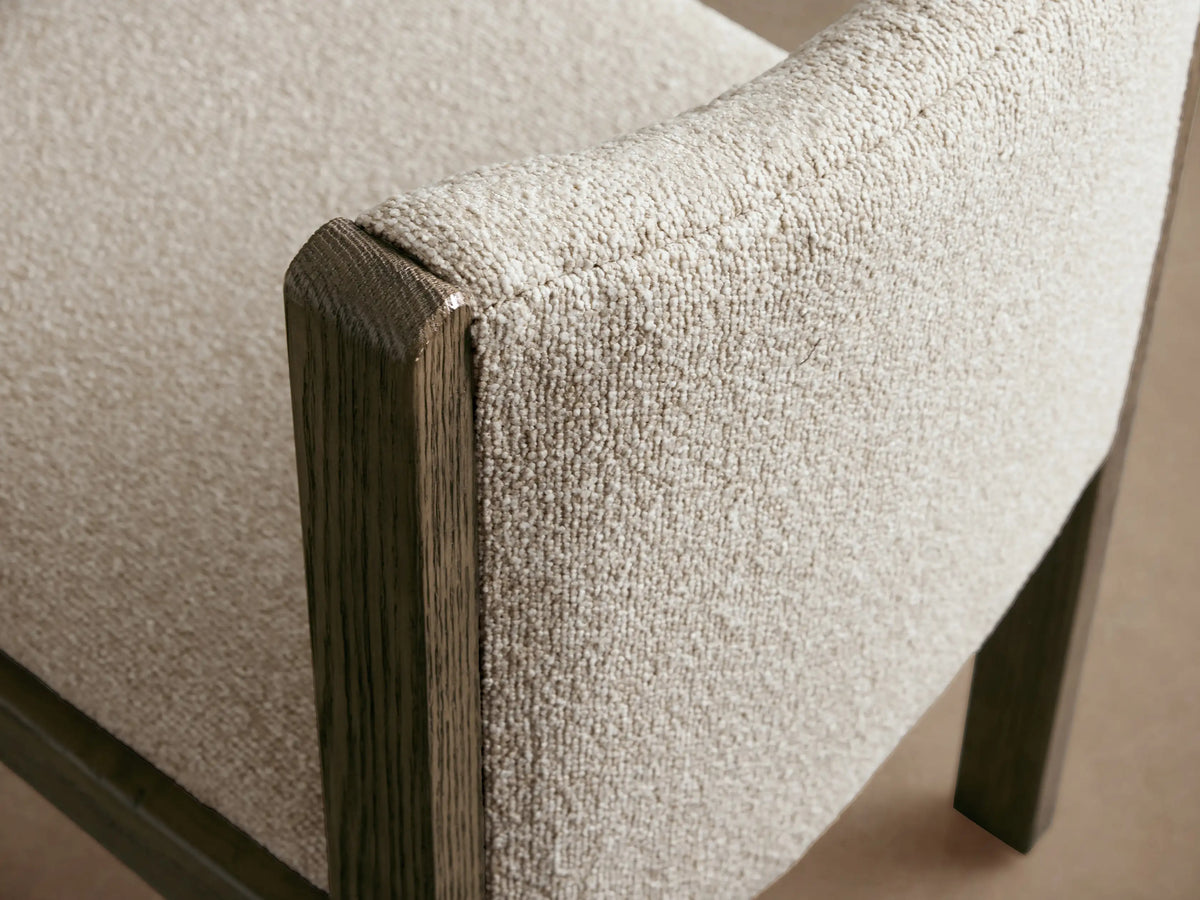 Paradiso Dining Chair, front view. Dark oak frame, light cream textured upholstery seat and curved back. On wood floor, beige wall.