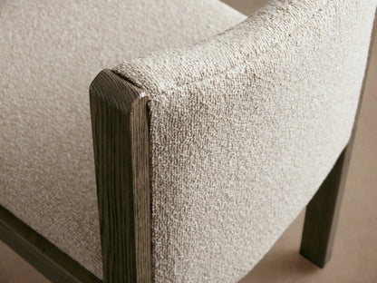 Paradiso Dining Chair, front view. Dark oak frame, light cream textured upholstery seat and curved back. On wood floor, beige wall.