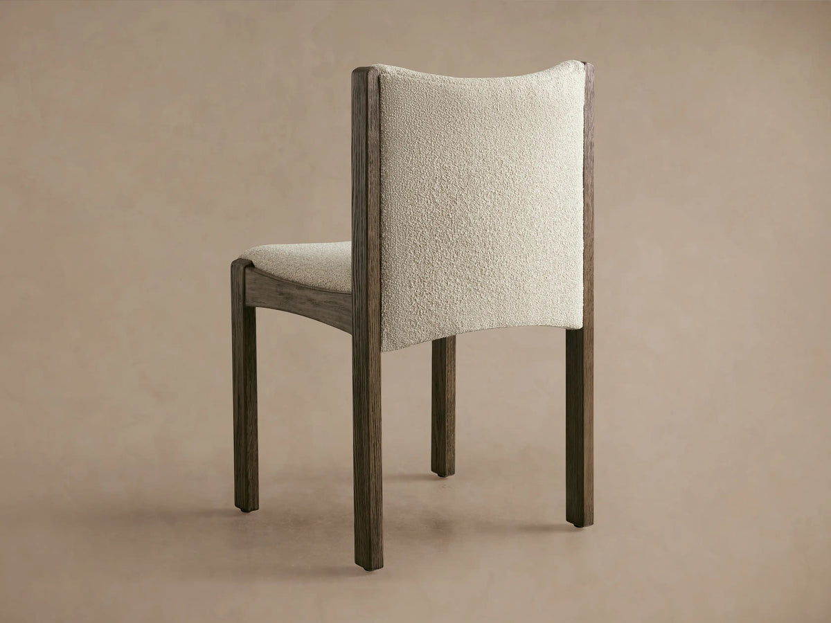 Close-up of Paradiso Dining Chair showing curved armrest with light beige textured upholstery and dark oak wood frame.