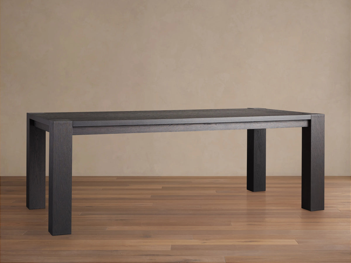 Parsons Dining Table crafted from dark Romanian oak wood with a rectangular top and thick rectangular legs, set on wooden floor.