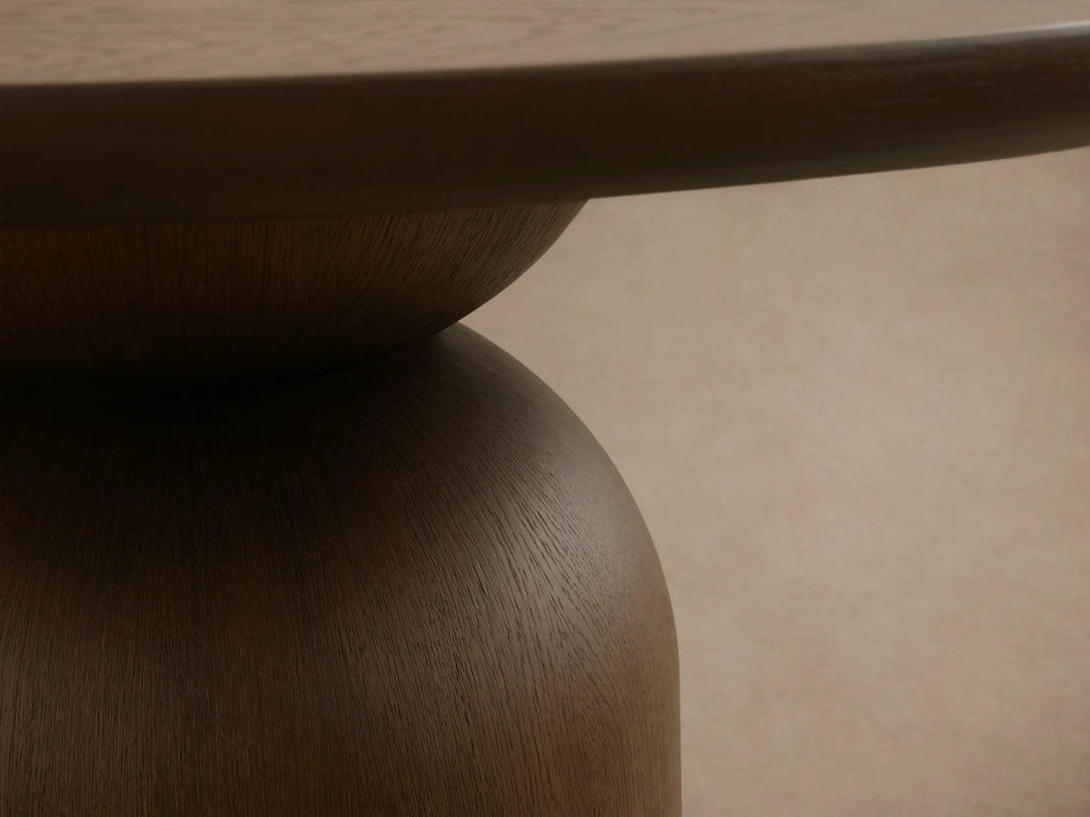 Dark wood Perth Round Dining Table with a thick circular top and a modern, sculptural pedestal base on a wood floor.