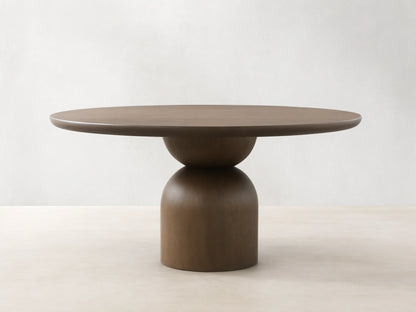 Dark wood Perth Round Dining Table with a thick circular top and a modern, sculptural pedestal base on a wood floor.