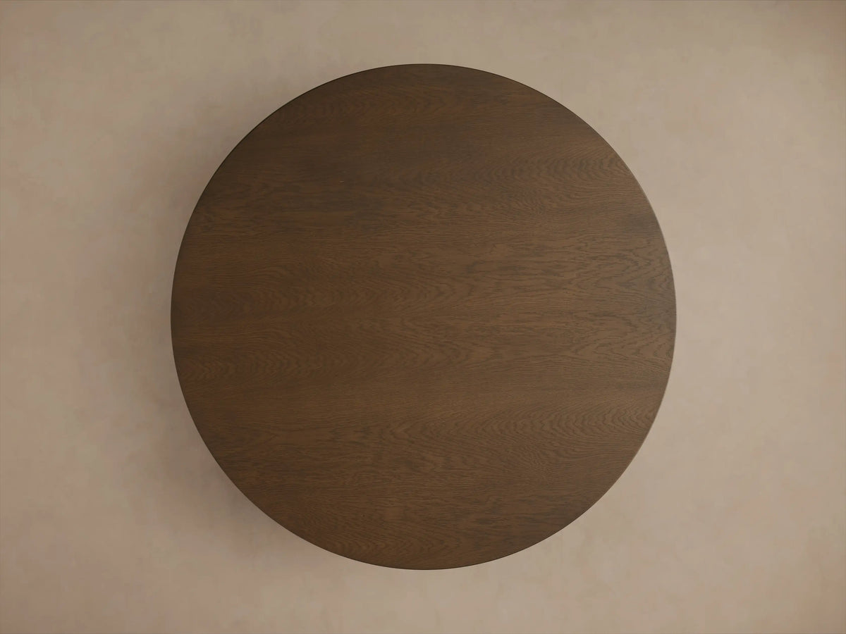 Close-up of Perth Round Dining Table. Dark brown wood grain visible on the round tabletop edge and curved pedestal base.
