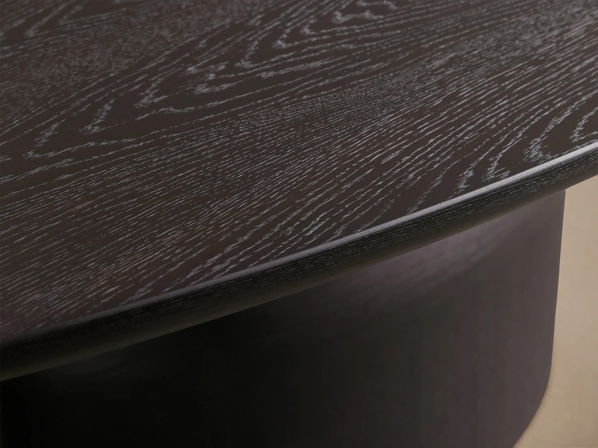 Dark espresso Perth Oval Dining Table, featuring a wide oval top on a unique, rounded pedestal base, against a neutral wall.