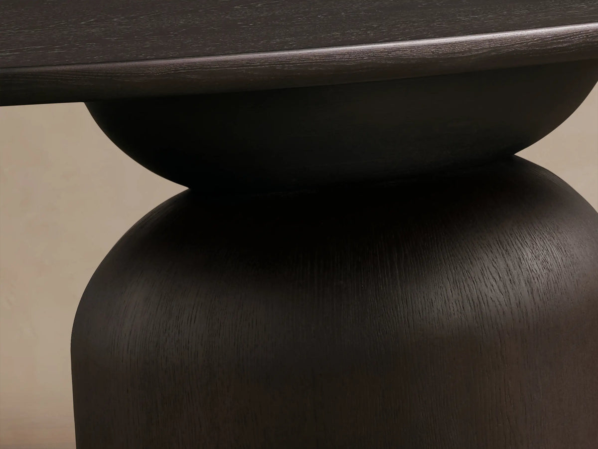 Perth Oval Dining Table, close-up of its dark ebony wood surface with visible grain, rounded edge, and dark curved base.
