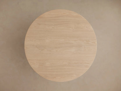 Close-up of Perth Round Dining Table. Light wood, round top, sculptural base with stacked inverted bowl and bell shapes.