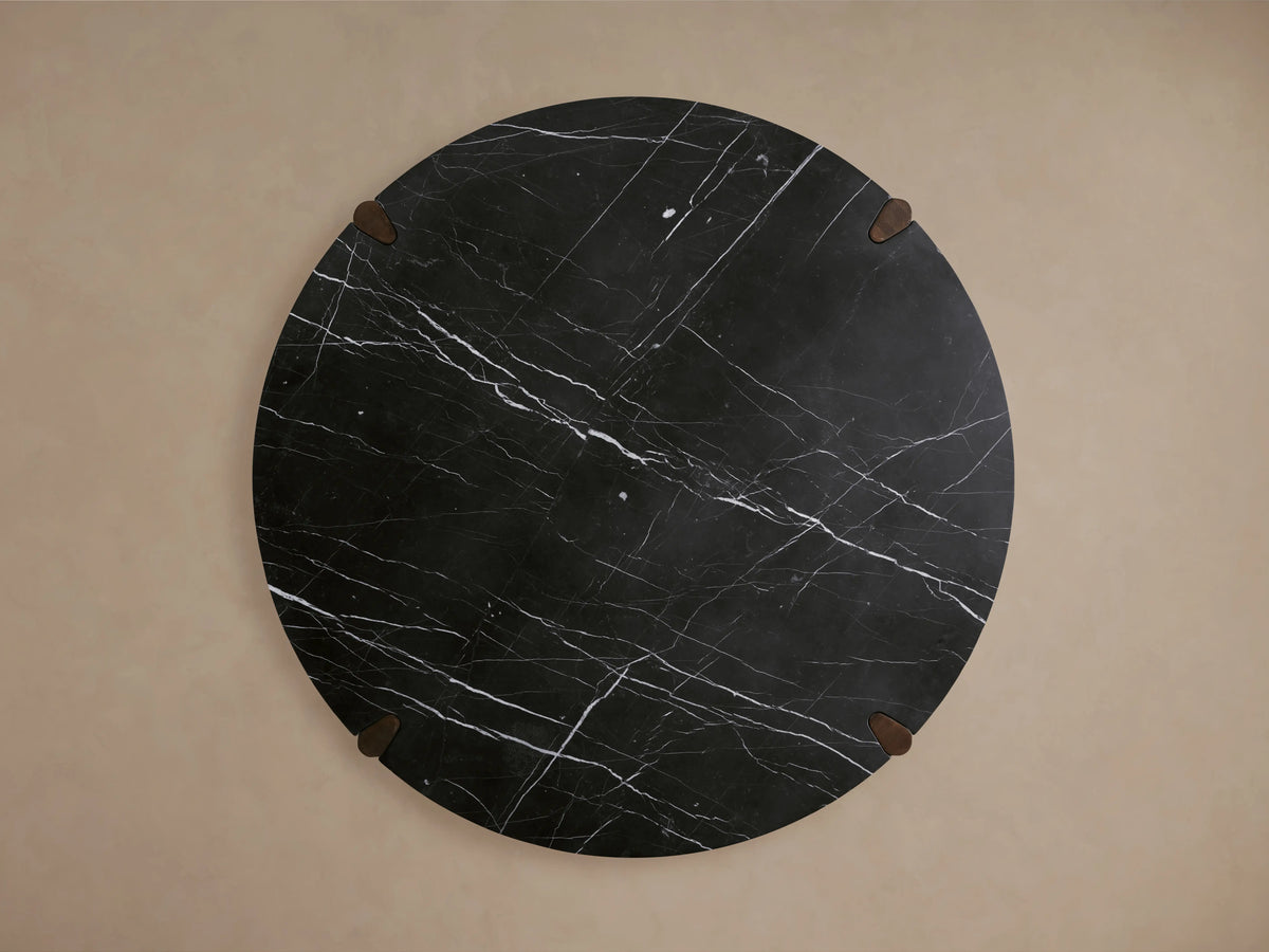 Round dining table with a black marble top featuring white veining, supported by solid red oak legs with a dark finish.