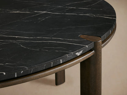 The Pyet Round Dining Table features a black marble top with white veining, supported by four round dark oak wood legs.
