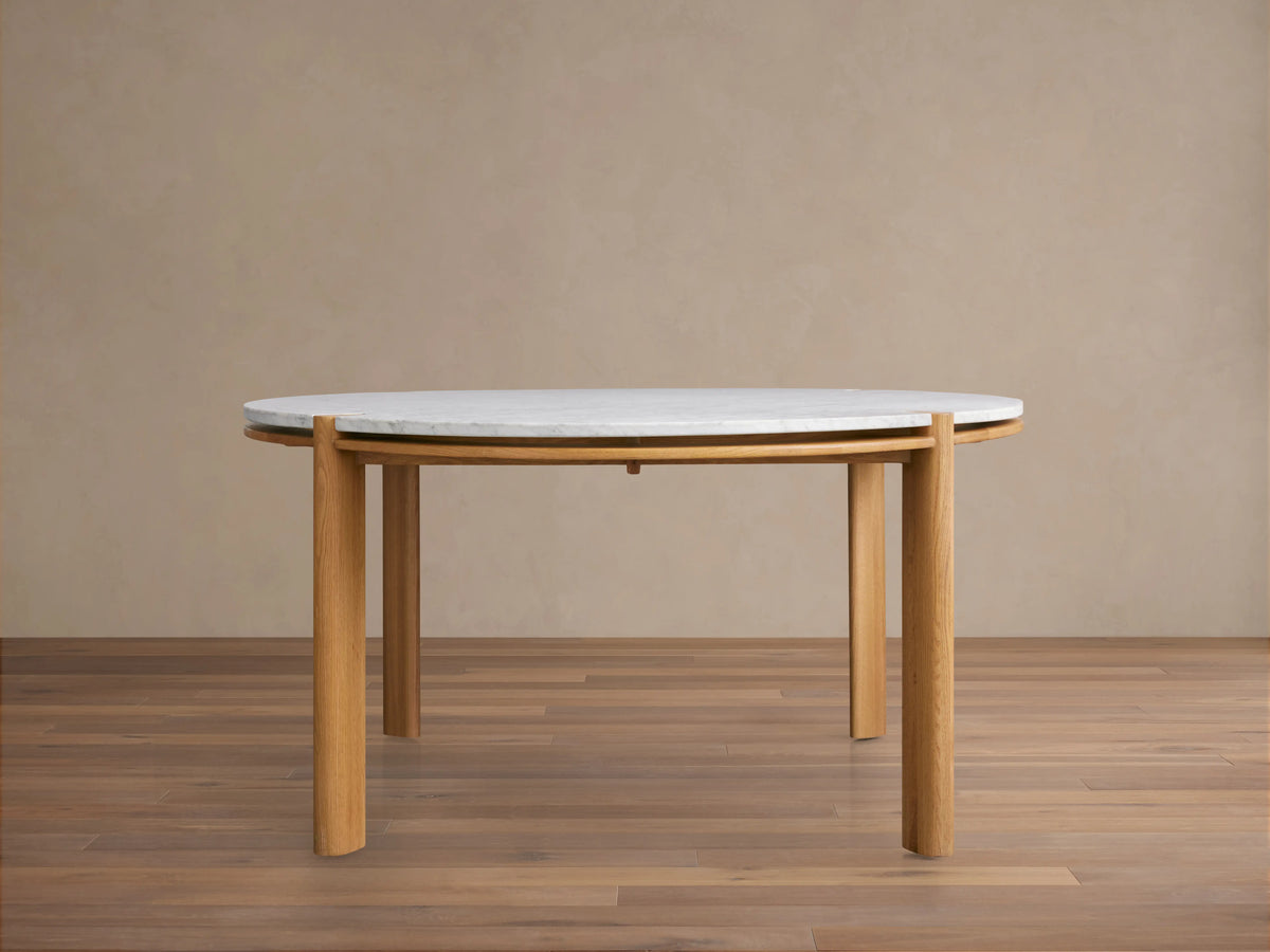 Pyet Round Dining Table with white Carrara marble top and four solid red oak wood legs on a wooden floor.