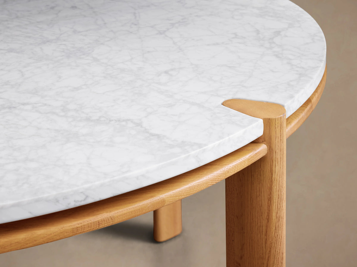 Pyet Round Dining Table with a white marble top and solid red oak wood base. The table is set on a wooden floor with a neutral background.