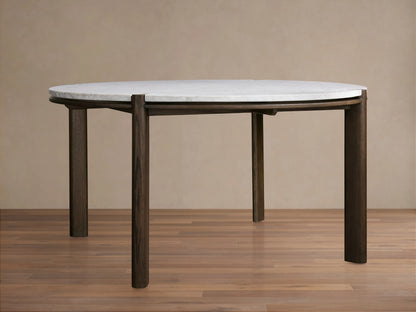 Pyet Round Dining Table with a white Carrara marble top and robust solid red oak legs, set on a wooden floor against a beige wall.