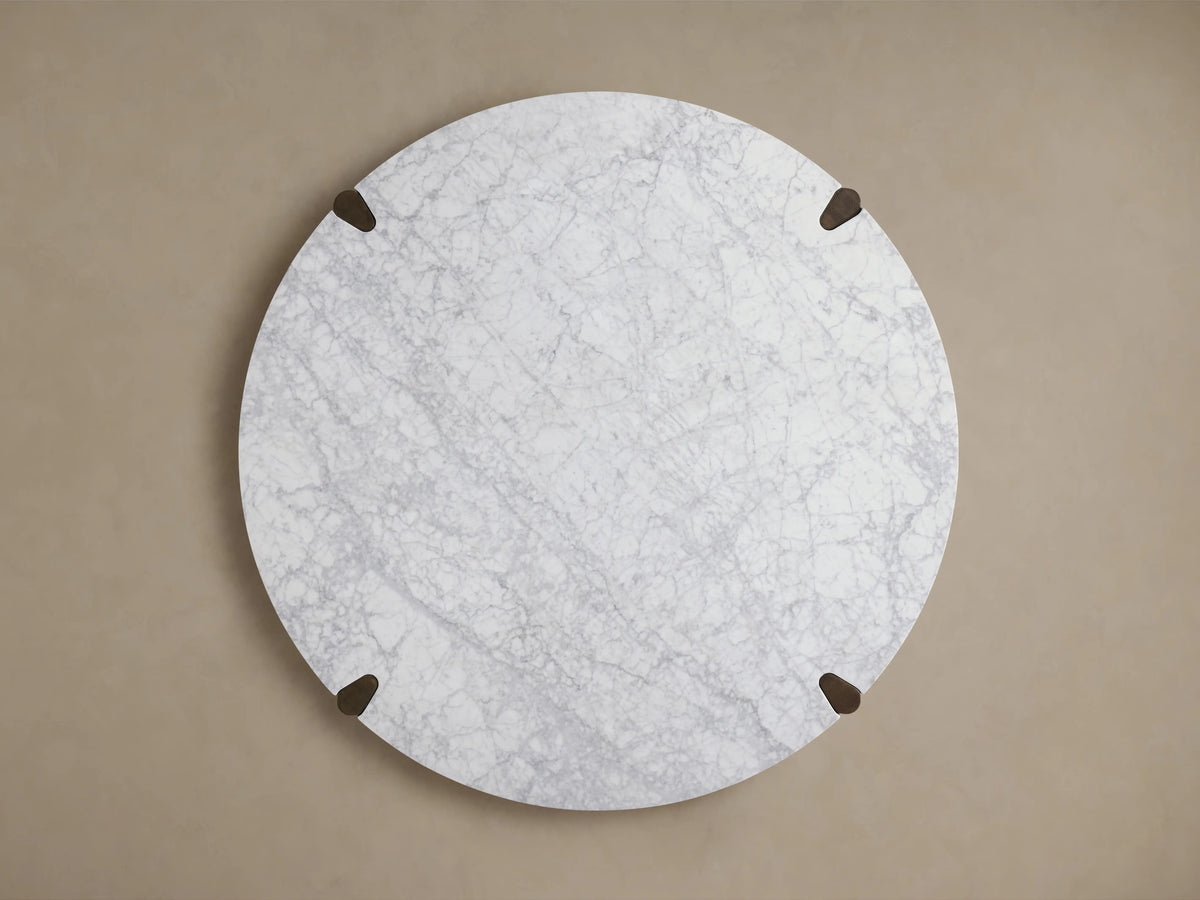 Round Pyet Dining Table features a white Carrara marble top with subtle gray veining, supported by dark red oak legs.