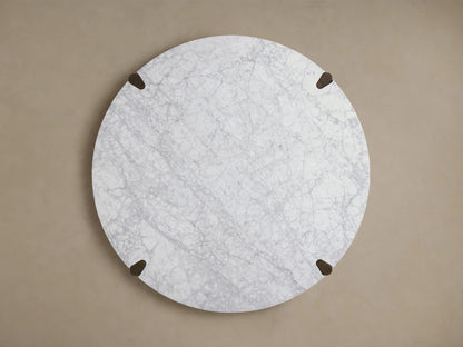 Round Pyet Dining Table features a white Carrara marble top with subtle gray veining, supported by dark red oak legs.