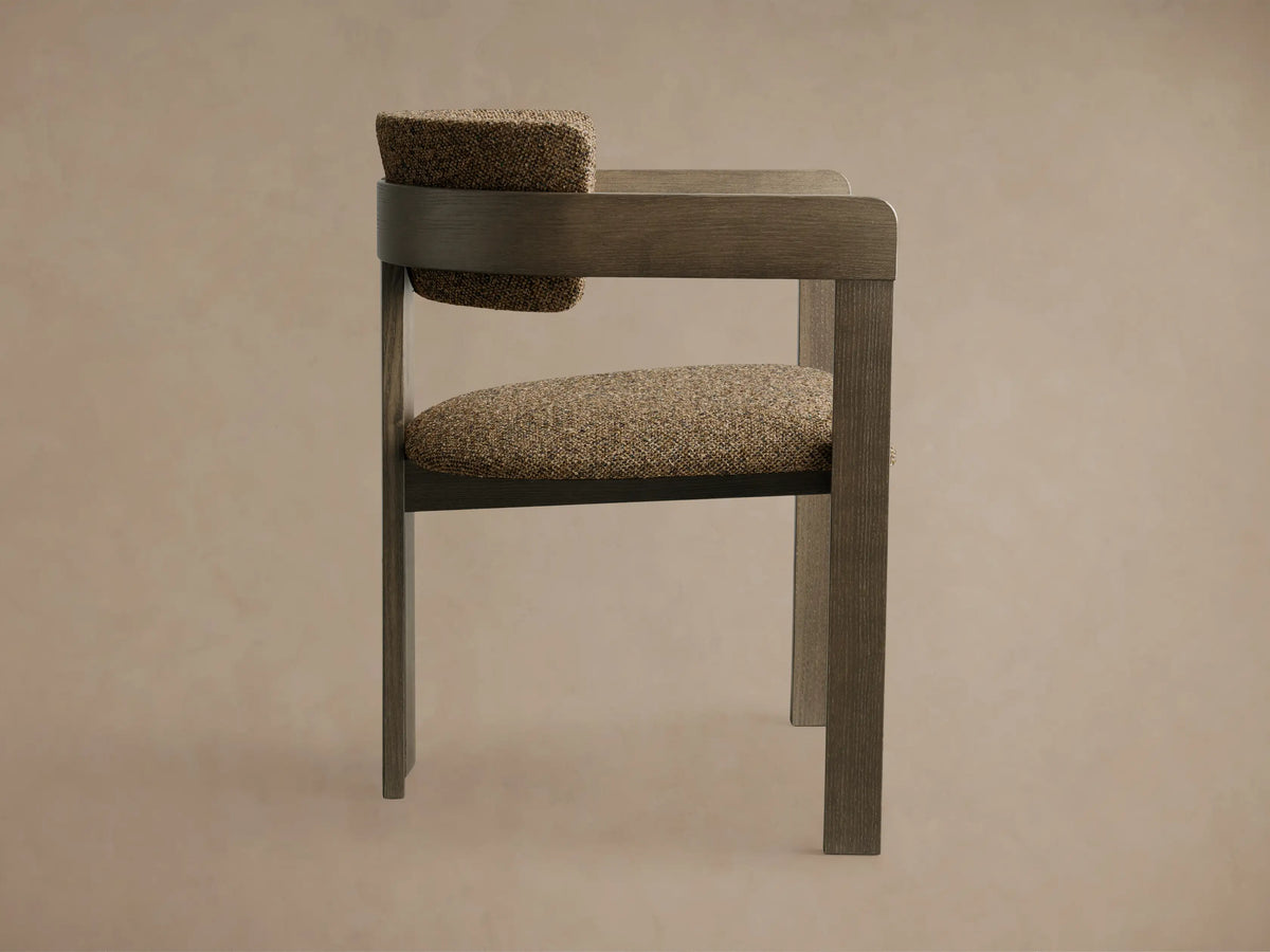 Side profile of the Rodin Dining Arm Chair, featuring a gray ash wood frame with speckled brown upholstered seat and backrest.