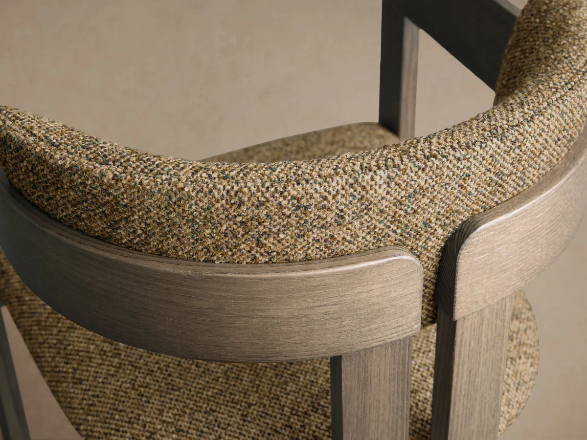 Close-up of the Rodin Dining Arm Chair, showing its curved gray ash wood frame and multi-tonal speckled beige fabric.