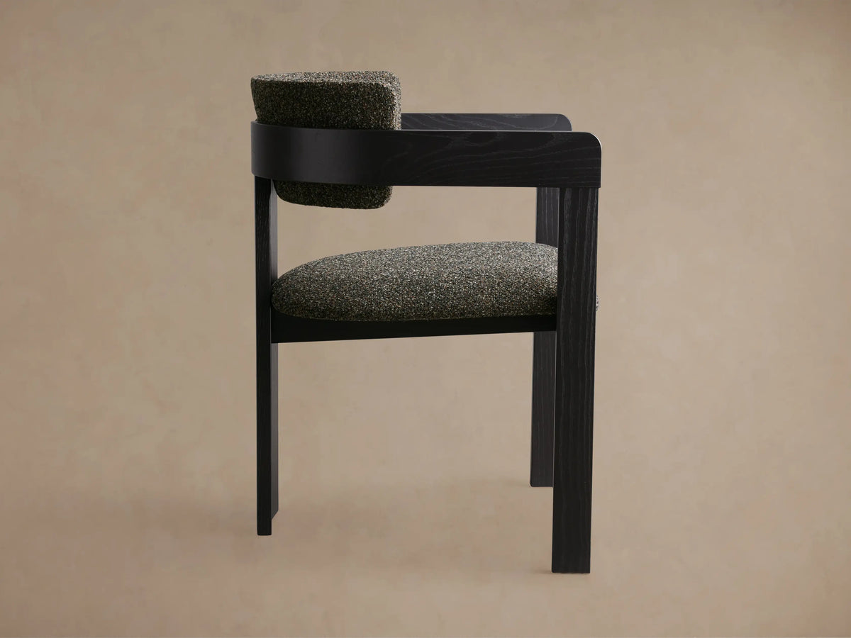 Close-up of the back and armrest of the Rodin Dining Arm Chair, featuring dark ash wood and textured gray-green upholstery.