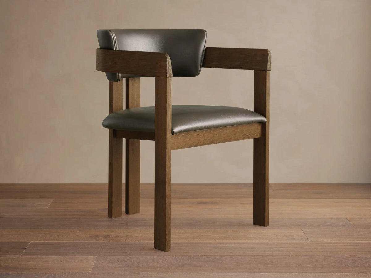Rodin Faux Leather Arm Chair. Dark brown wooden frame with dark gray faux leather seat and back, angled on wood floor.
