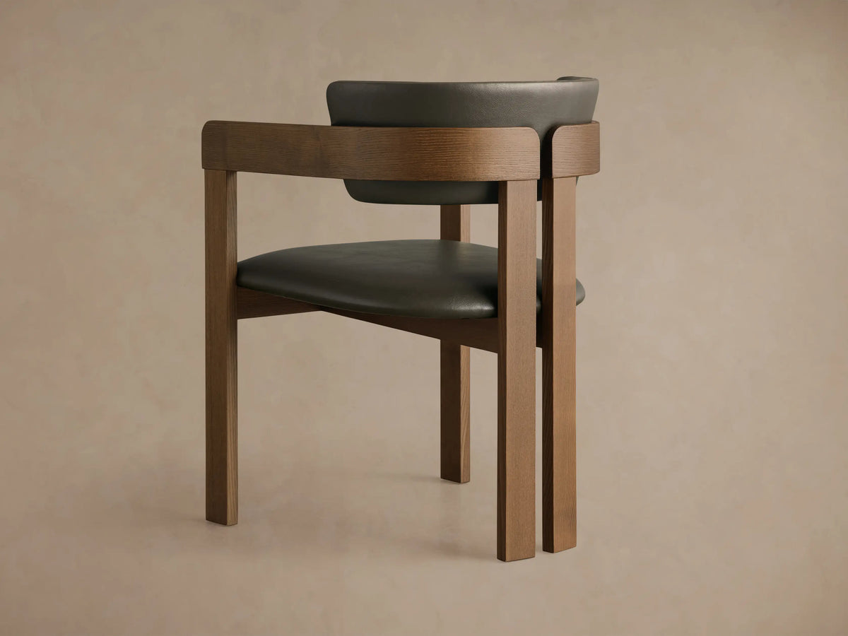 Close-up of Rodin Faux Leather Arm Chair, showing curved dark brown faux leather backrest and seat against a warm ash wood frame.