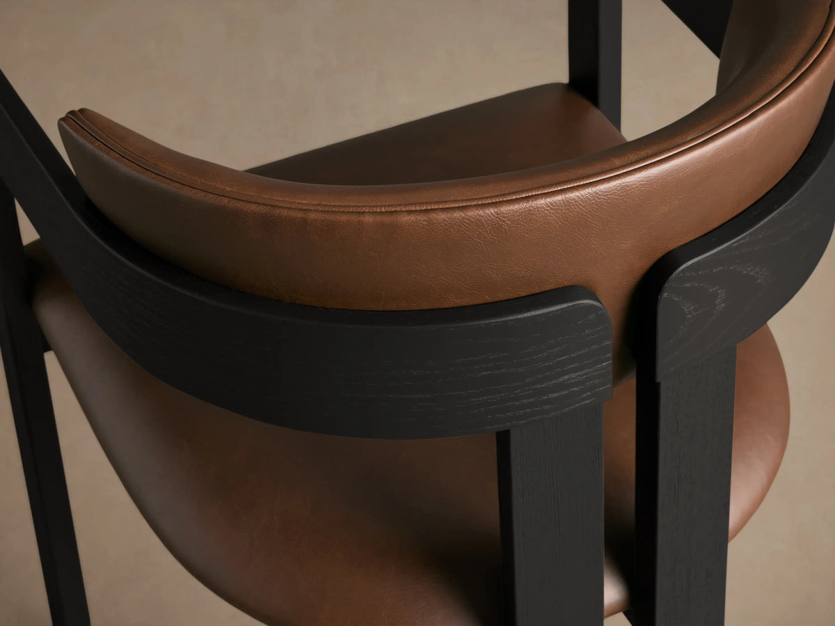 Rodin Faux Leather Arm Chair. Front view of black ash wood frame with brown padded seat and backrest, studio shot.