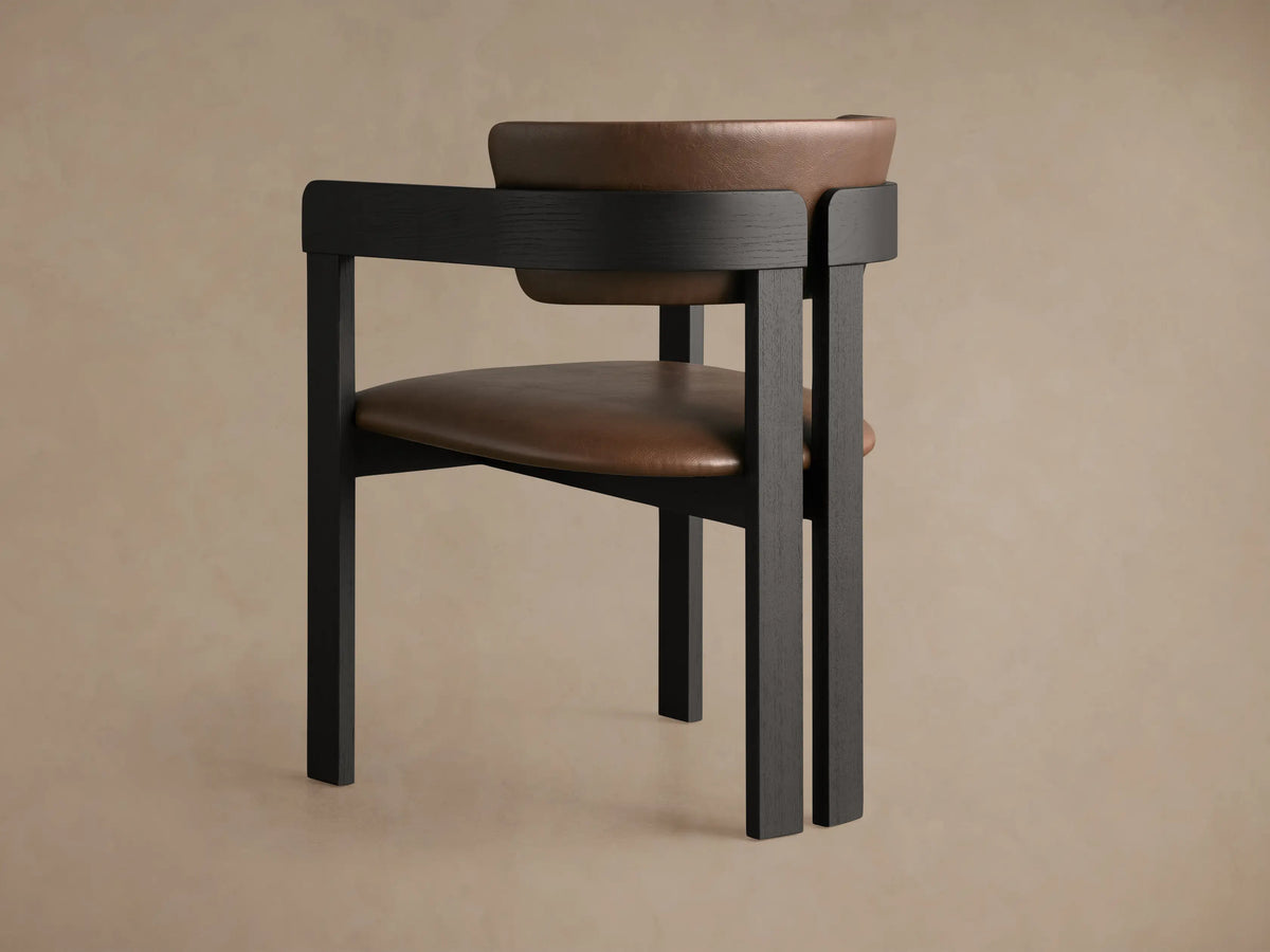 Close-up of Rodin Faux Leather Arm Chair with dark wooden frame, showing curved brown faux leather armrest and back.
