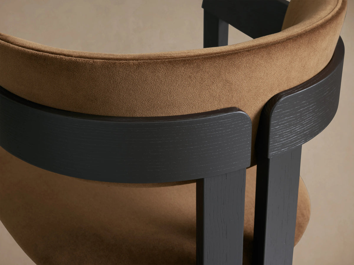 Rodin Dining Arm Chair in front view, with brown cushioned seat and backrest, dark ash wood frame, on wooden floor.