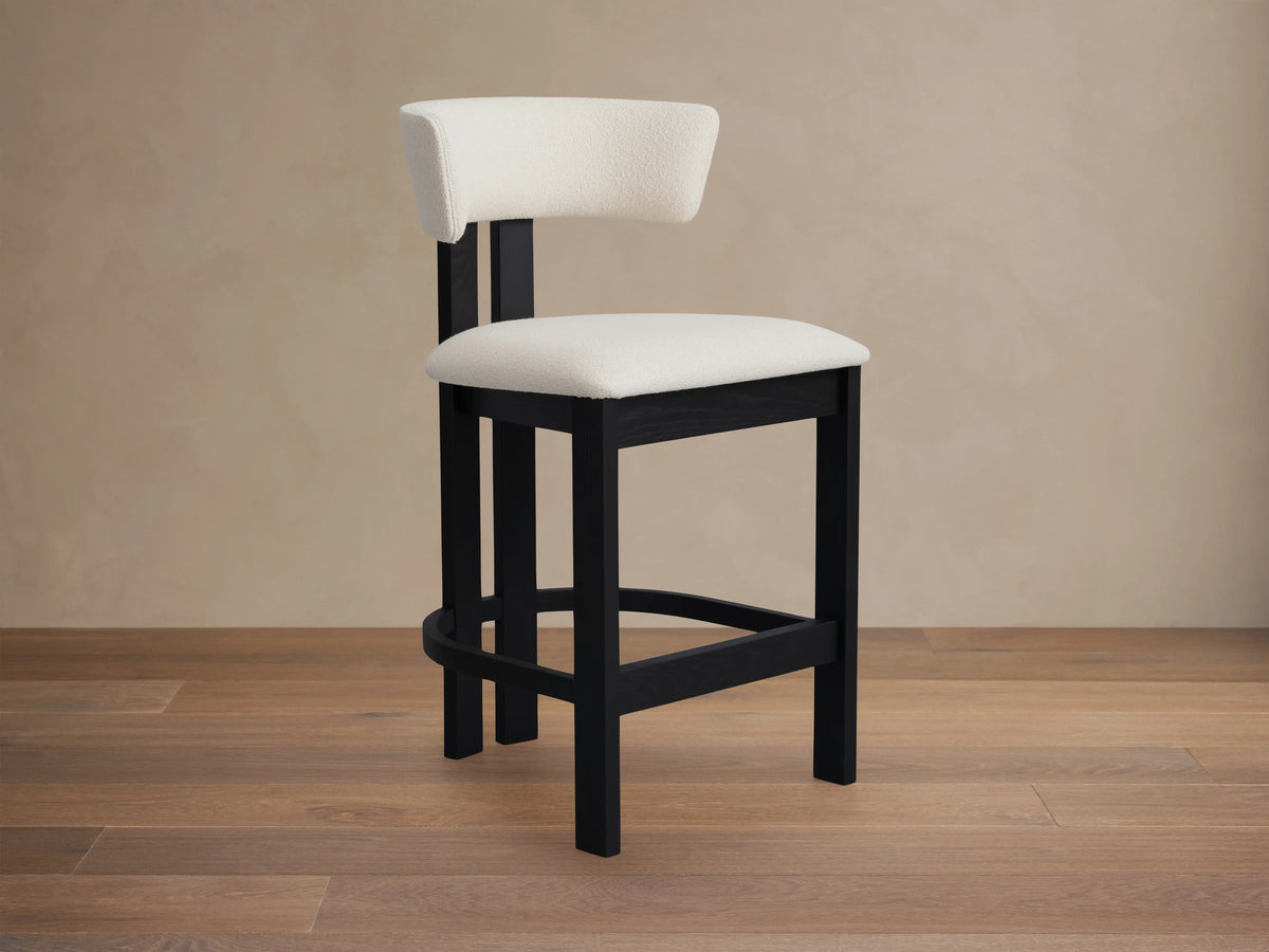Rodin Armless Stool in ash wood with a black frame, cream cushioned seat and backrest, set on hardwood floor with neutral wall.