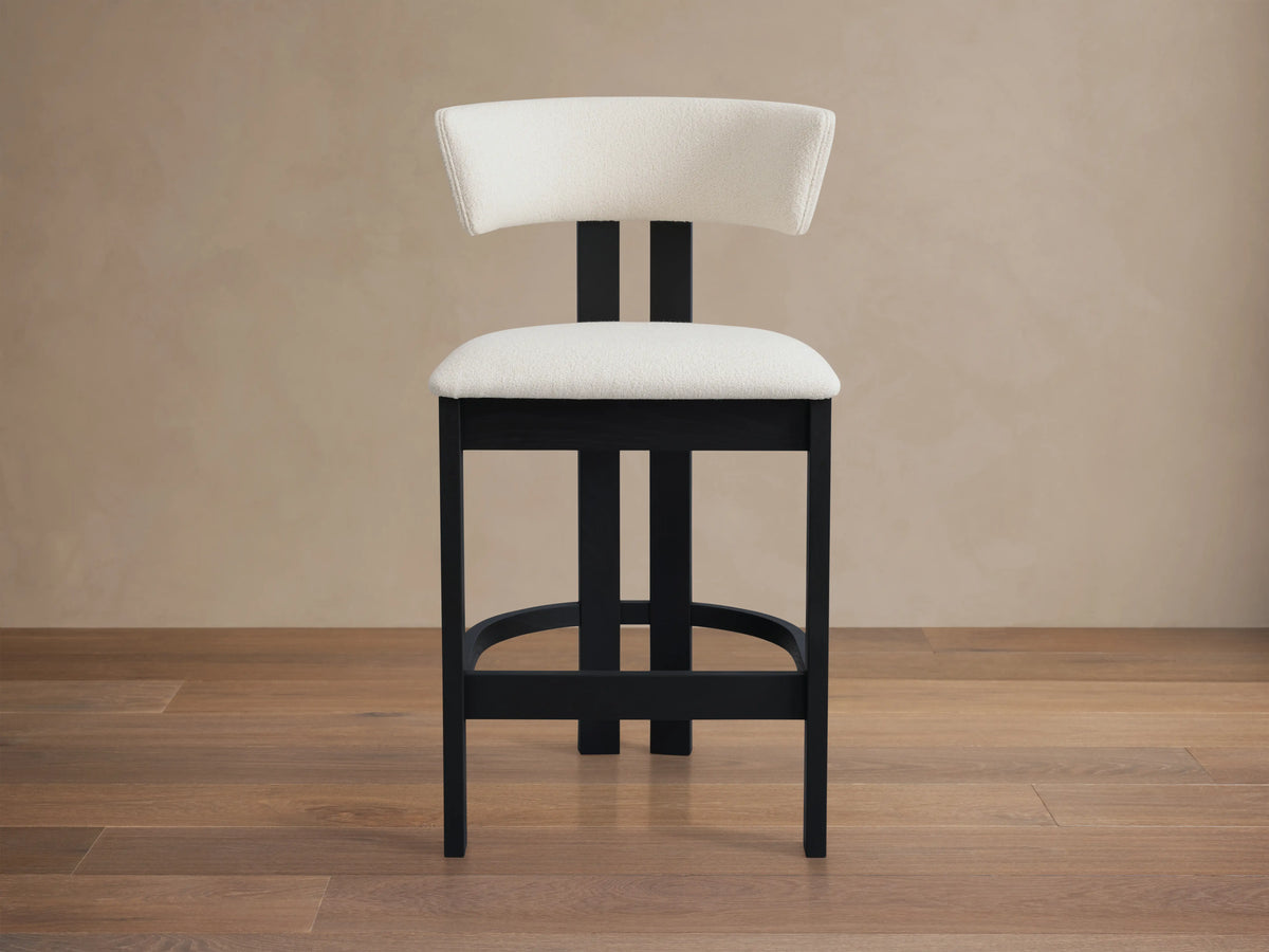 Rodin Armless Stool in ash wood with a black frame, cream cushioned seat and backrest, set on hardwood floor with neutral wall.