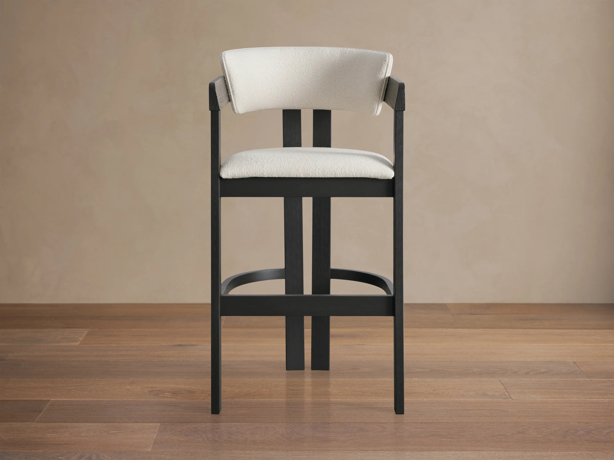Rodin Stool with dark ash wood frame, cream cushion and backrest, soft fabric, on a wooden floor against a neutral wall.