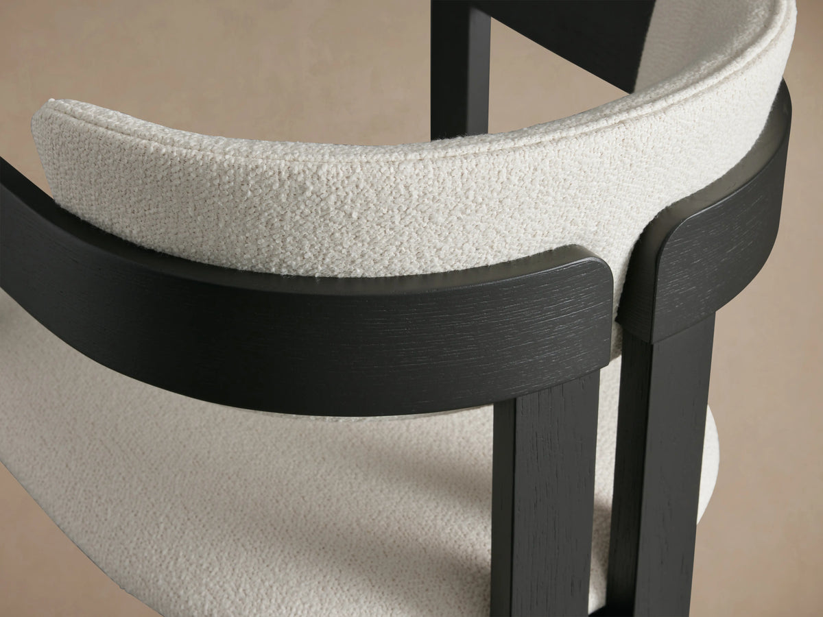 Rodin Stool made in Italy with dark ash wood frame and cream cushion. Front view on wooden floor with neutral wall background.
