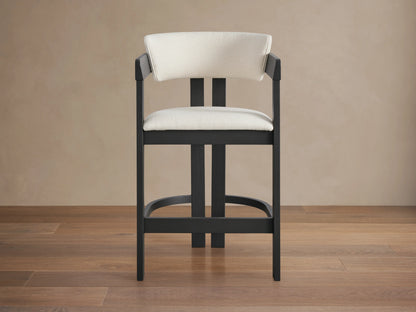 Rodin Counter Stool with cream upholstered seat and back, black ash wood frame, placed on a wooden floor against a beige wall.