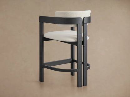 Rodin Counter Stool in a dark ash wood frame with a curved backrest and seat upholstered in light fabric, shown on a beige background.