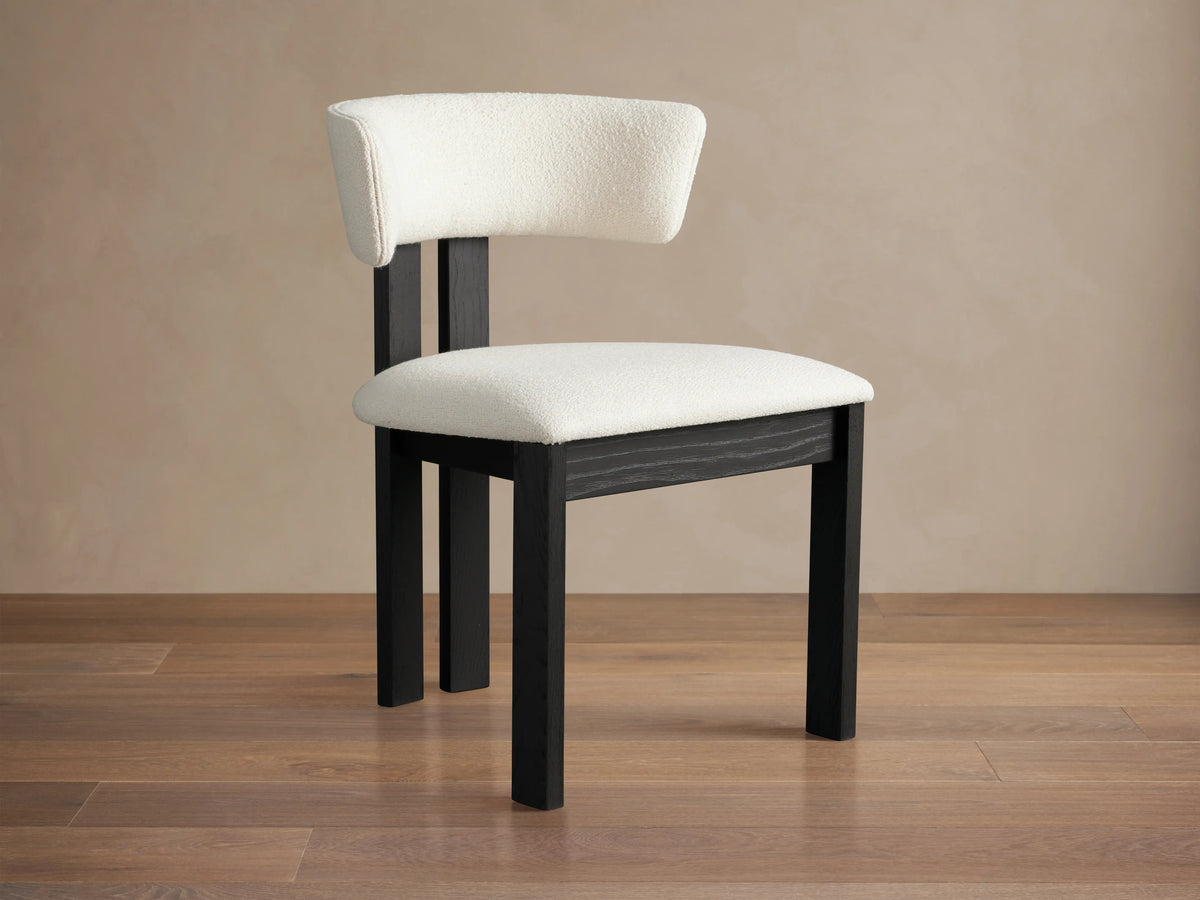 Rodin Dining Side Chair with a curved backrest and cushioned seat in white fabric, set on dark ash wood legs on a wooden floor.