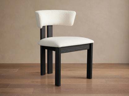 Rodin Dining Side Chair with a curved backrest and cushioned seat in white fabric, set on dark ash wood legs on a wooden floor.