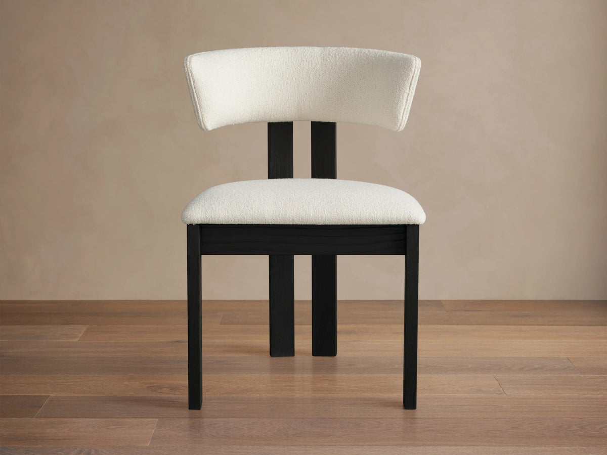 Rodin Dining Side Chair with a curved backrest and cushioned seat in white fabric, set on dark ash wood legs on a wooden floor.