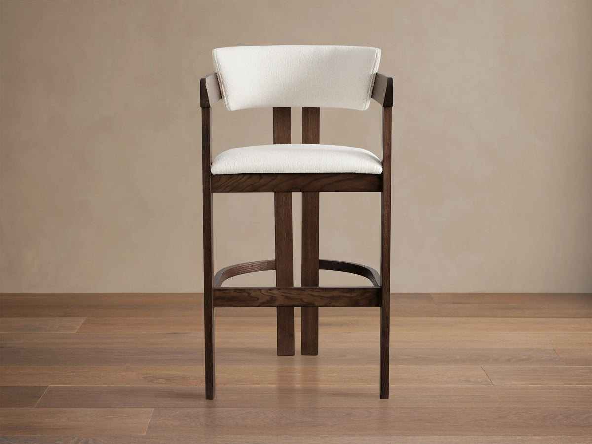 Rodin Stool made from dark ash wood with a cream cushioned seat and backrest. Features a circular footrest on wooden floor.