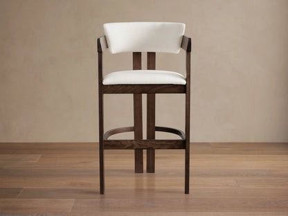Rodin Stool made from dark ash wood with a cream cushioned seat and backrest. Features a circular footrest on wooden floor.