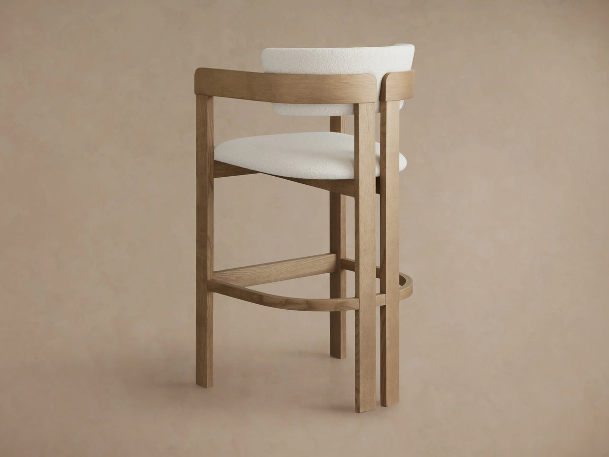 Rodin Barstool in Natural, featuring a round seat upholstered in textured cream fabric, surrounded by natural ash wood backrest and legs.