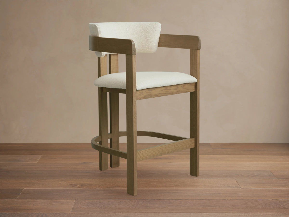 Rodin Counter Stool in Natural, ash wood frame with light upholstery, angled view. Features curved backrest, cushioned seat, footrest.