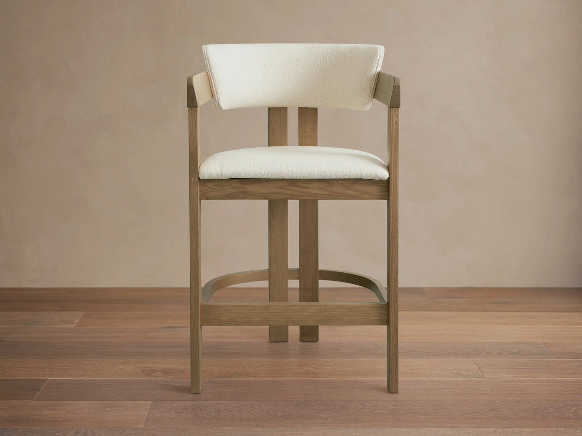 Rodin Counter Stool in Natural, ash wood frame with light upholstery, angled view. Features curved backrest, cushioned seat, footrest.