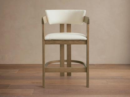 Rodin Counter Stool in Natural, ash wood frame with light upholstery, angled view. Features curved backrest, cushioned seat, footrest.