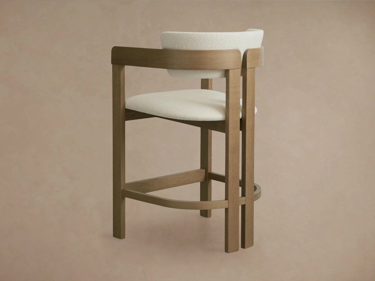 Rodin Counter Stool in Natural, featuring an ash wood frame with a curved backrest. Upholstered in soft, off-white performance fabric.