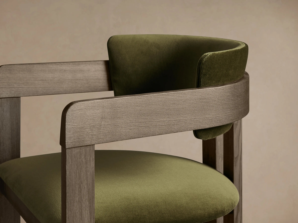 Rodin Dining Arm Chair in Vance Olive, ash wood frame, olive green cushioned seat and backrest, on a wooden floor.
