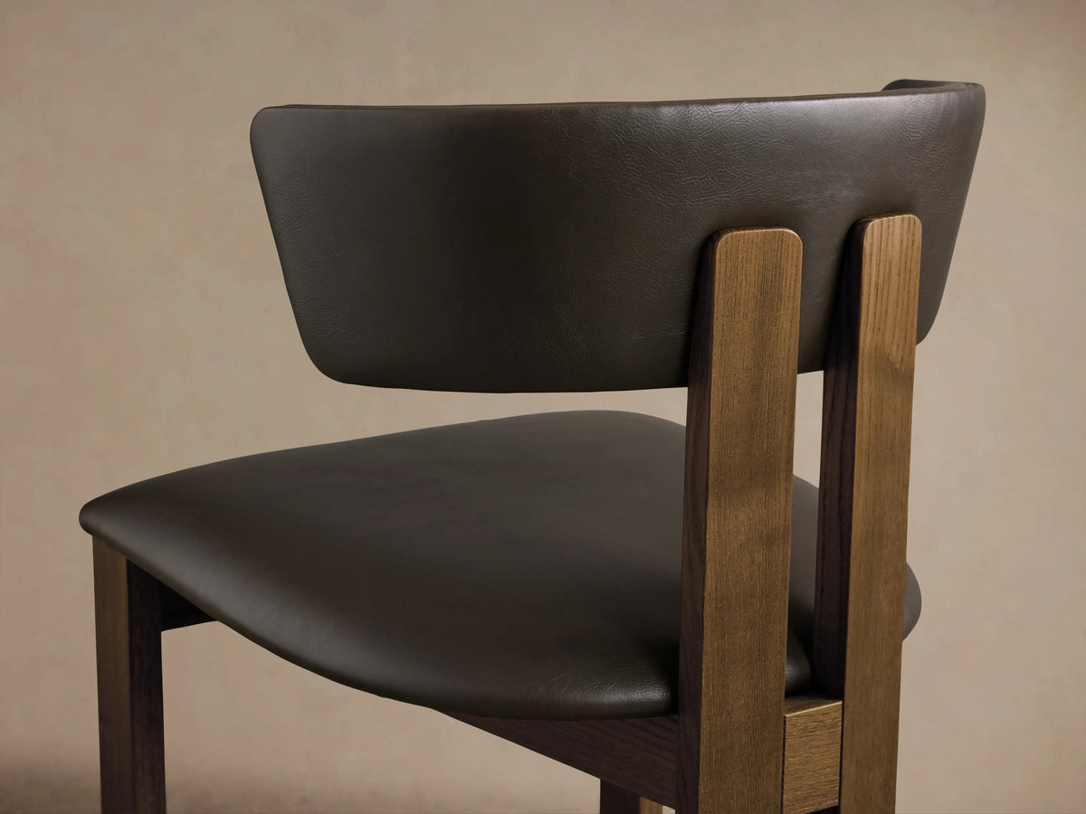 Rodin Faux Leather Dining Side Chair. Front view of dark brown faux leather seat/back and dark ash wood frame on wood floor.