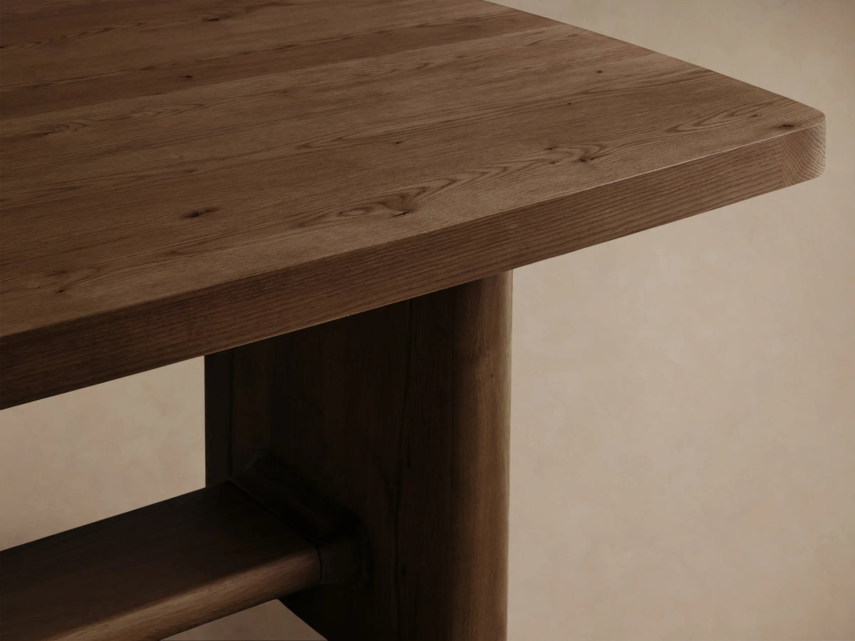 Close-up of the dark brown wooden table, showcasing its natural wood grain, rounded tabletop edge, and sturdy, thick leg.