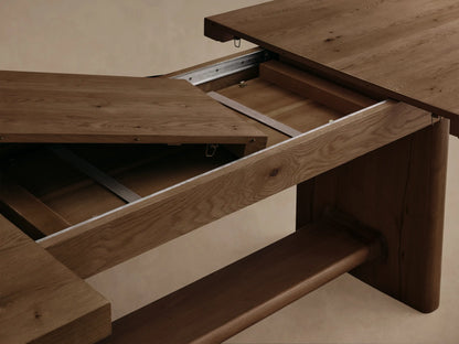 Close-up of a natural wood extendable dining table with a leaf being added, revealing the metal extension slides and internal mechanism.