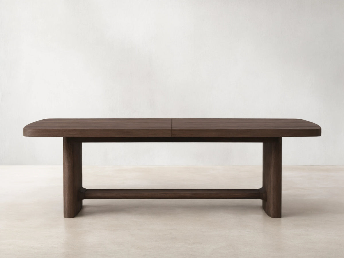 Front view of a dark brown wooden dining table with rounded corners, a central seam, and thick block legs connected by a stretcher.