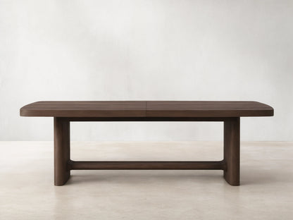 Front view of a dark brown wooden dining table with rounded corners, a central seam, and thick block legs connected by a stretcher.